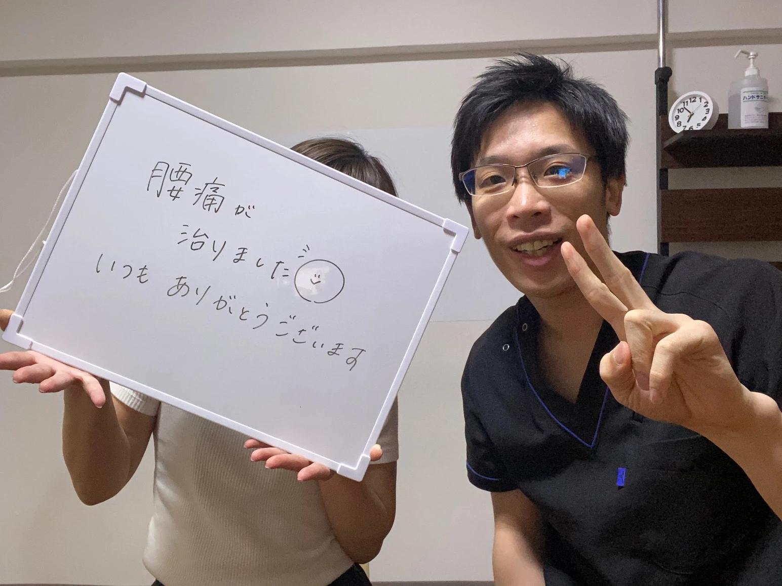 腰痛についての感謝のメッセージを書いたホワイトボードを持つ手島様と整体院心華の施術者